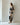 A woman stands in profile wearing a black and beige abstract floral print matching set with a matching patterned belt and black flat sandals, set against a minimalist off-white studio background.