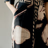 A close-up of a person wearing a black trousers with a large abstract cream and red print, paired with a matching patterned tie belt.