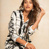 A woman wearing a black and white abstract patterned long-sleeve shirt dress, posing against a neutral beige textured wall.