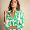 A woman wearing a green and white patterned button-up shirt dress, posing against a textured beige background.
