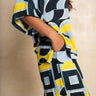A woman wearing a loose, short-sleeve top and matching pants with a bold abstract geometric print in yellow, navy blue, and light blue, standing against a neutral beige textured wall.